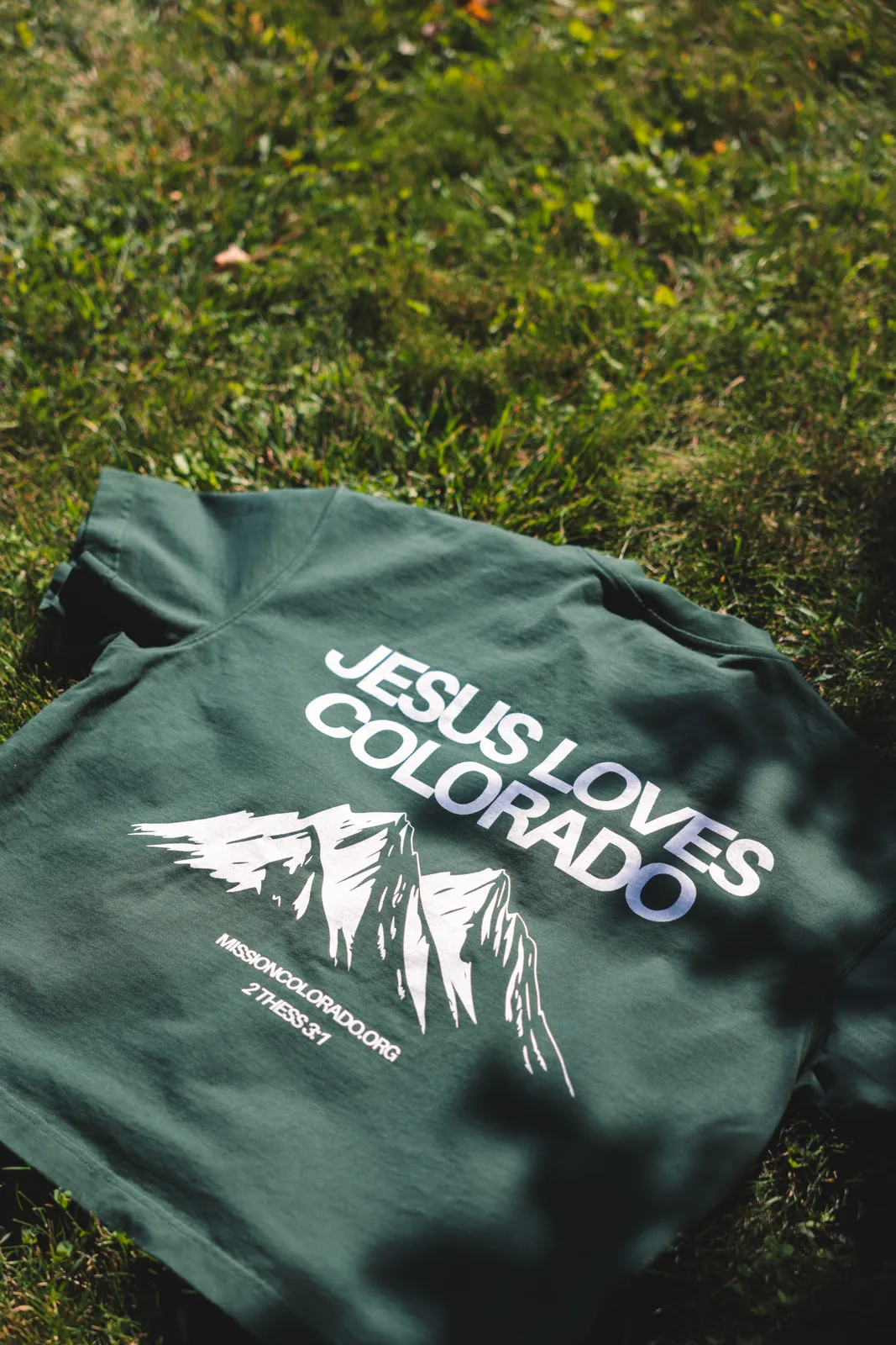 Green tee reading Jesus Loves Colorado with a mountain range illustration